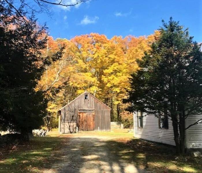 an old barn with dirt driveway, trees with bright yellow and orange leaves and a blue sky