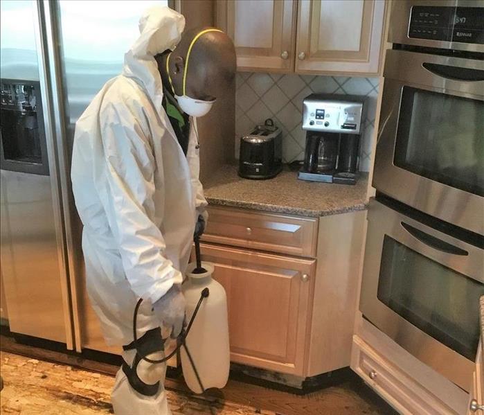 man in protective gear spraying the floor of a kitchen